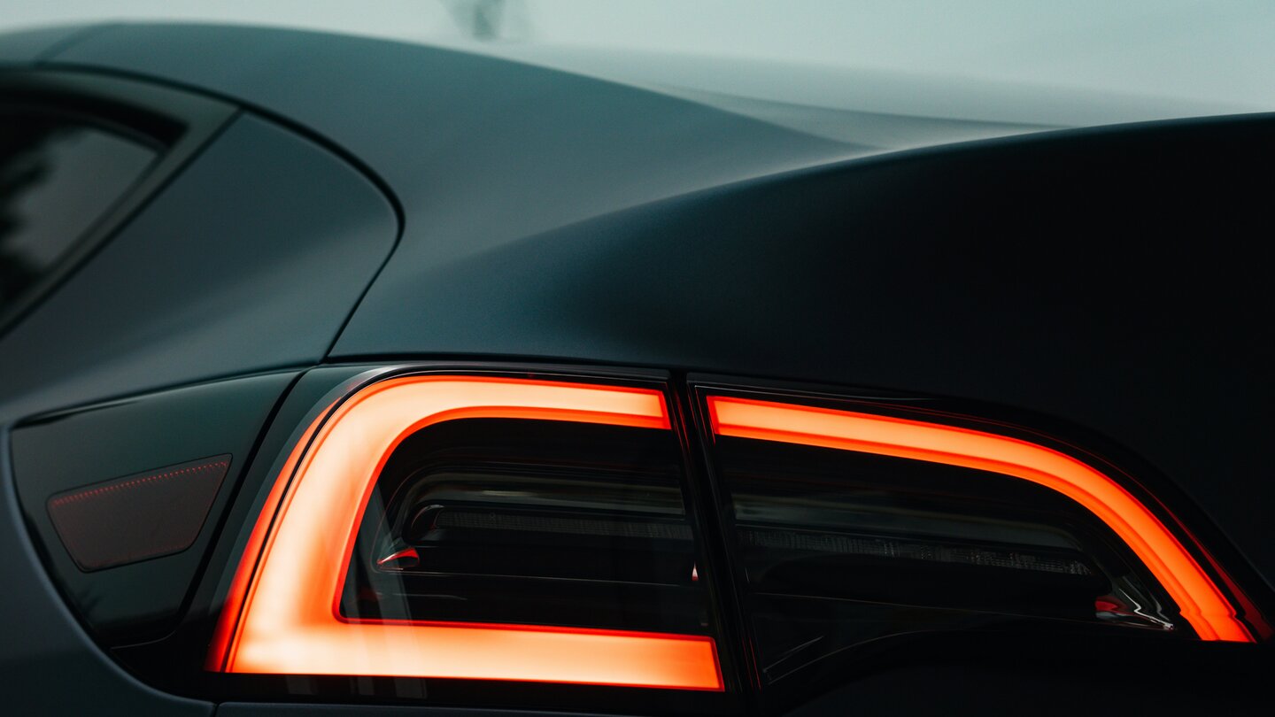 Nahaufnahme leuchtende Rückleuchte eines matten dunkelgrauen Tesla